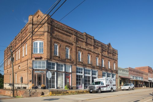 Historic brick building on a sunny street, featuring large windows and an ambulance parked nearby.