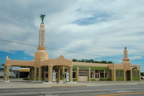 Art Deco-style Conoco gas station with tall, decorative towers and vintage gas pumps under a cloudy sky.