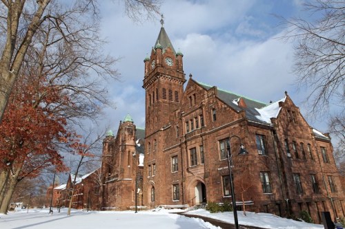 Historic building with a clock tower, surrounded by snow and bare trees under a cloudy sky.