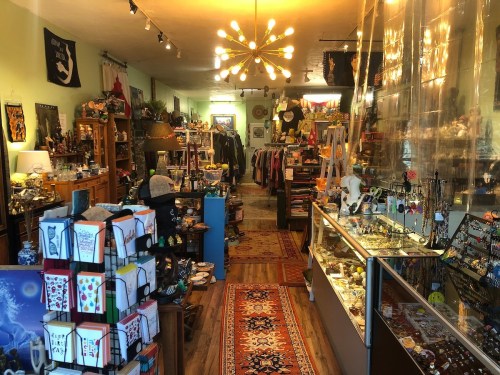 A cozy shop filled with eclectic items, including clothing, jewelry, and decorative pieces, with warm lighting and wooden floors.