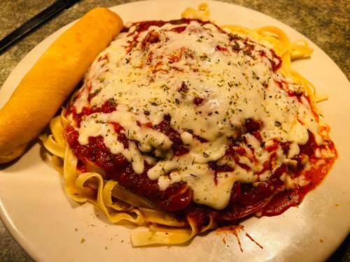 A plate of fettuccine topped with marinara sauce and melted cheese, accompanied by a breadstick.