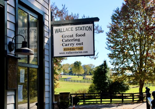 Sign for Wallace Station featuring "Great food, Catering, Carry out" with a scenic outdoor view.