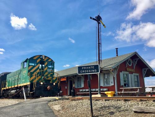 A vintage green and yellow train at a red train station under a blue sky with clouds, featuring a private crossing sign.