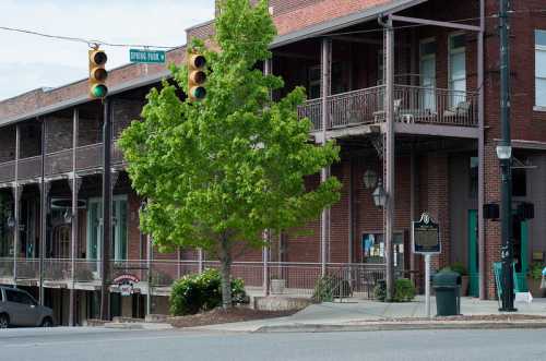 Historic brick buildings with balconies, a green tree, and traffic lights on a street corner.