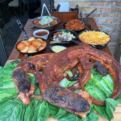 A large spread of food featuring smoked meats, sides, and rolls on a wooden table, garnished with lettuce.