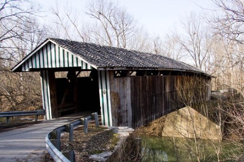 A rustic covered bridge with a wooden structure and striped sides, surrounded by bare trees and a quiet landscape.