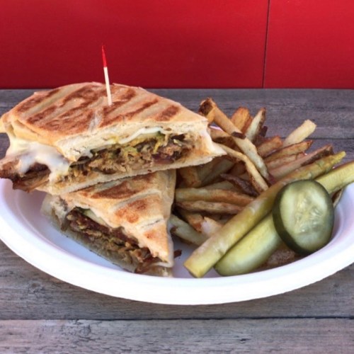 A plate with a grilled sandwich, fries, and pickles, garnished with a toothpick.