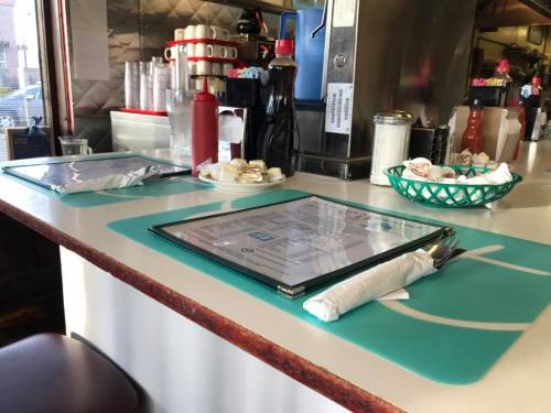 A diner table set with menus, napkins, condiments, and a basket of sugar packets.