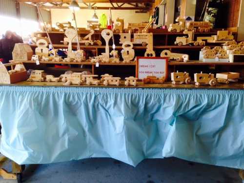 A display of various wooden toy vehicles and shapes on a table, covered with a light blue cloth.