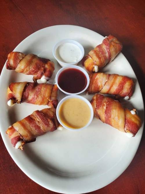 A plate of bacon-wrapped rolls with three dipping sauces in small cups.