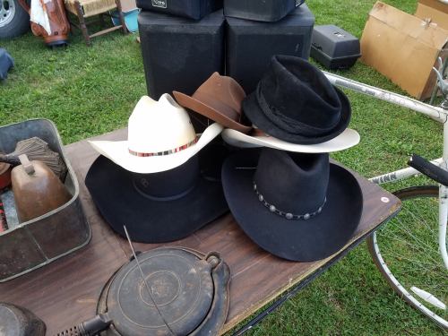 A collection of three cowboy hats in various colors displayed on a wooden table outdoors.
