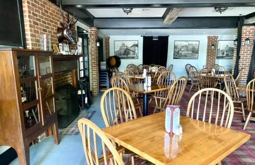 Cozy restaurant interior with wooden tables, chairs, and brick walls, featuring vintage artwork and a fireplace.
