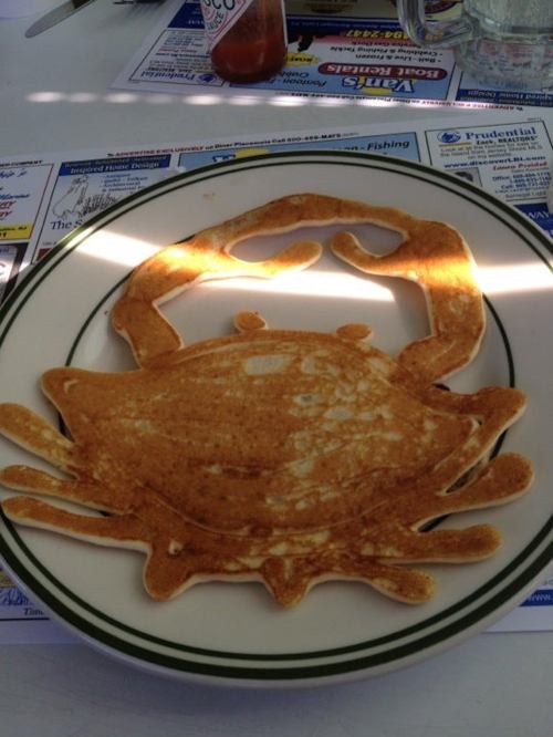 A large pancake shaped like a crab, served on a white plate with a green rim.