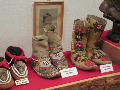 Display of traditional Native American footwear, including Northern Cree and Shoshone boots, with decorative designs.