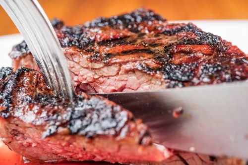 A close-up of a perfectly cooked steak being sliced, showcasing its juicy interior and charred exterior.
