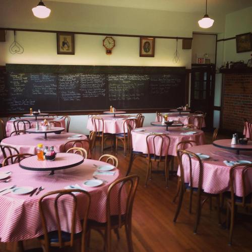 Cozy restaurant interior with checkered tablecloths, empty tables, and a chalkboard menu on the wall.