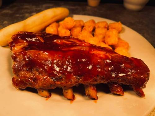 A plate featuring BBQ ribs with sauce, tater tots, and a banana on the side.