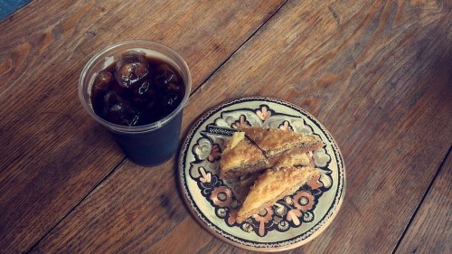 A cup of iced coffee next to a plate of baklava on a wooden table.