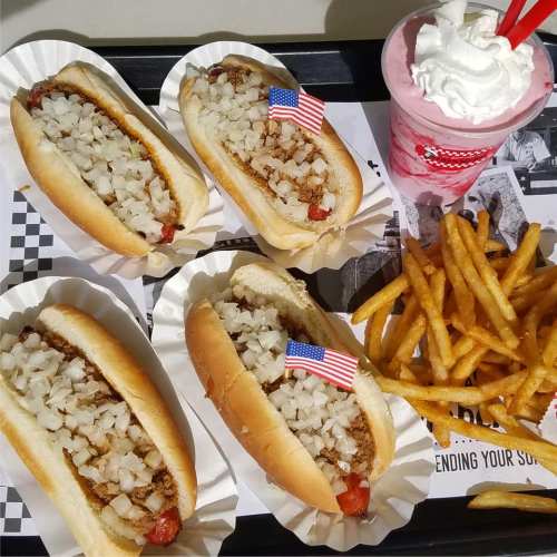 Four hot dogs topped with onions and small American flags, served with fries and a strawberry milkshake.
