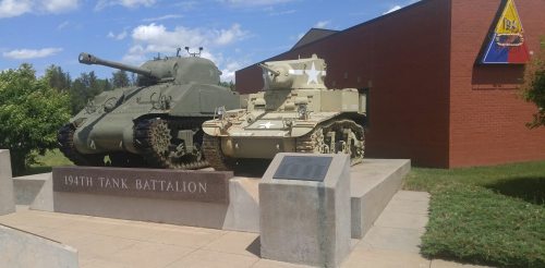 Two military tanks displayed at the 194th Tank Battalion memorial, set against a blue sky and green grass.