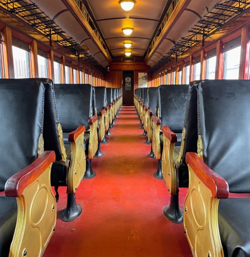 Interior of a vintage train car featuring rows of black seats and a polished wooden finish.