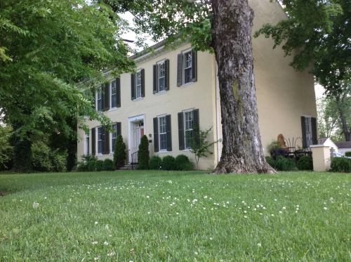 A yellow two-story house with black shutters, surrounded by green grass and trees.
