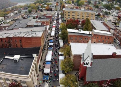 Aerial view of a bustling street market with tents, surrounded by colorful autumn trees and historic buildings.