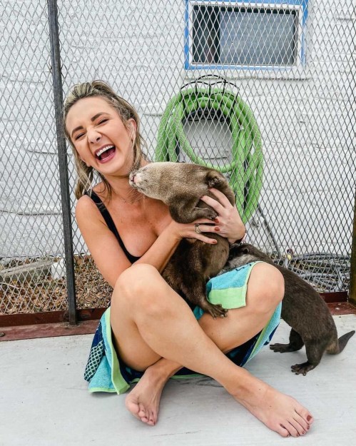 A woman laughs while playfully interacting with a friendly animal in a fenced area.
