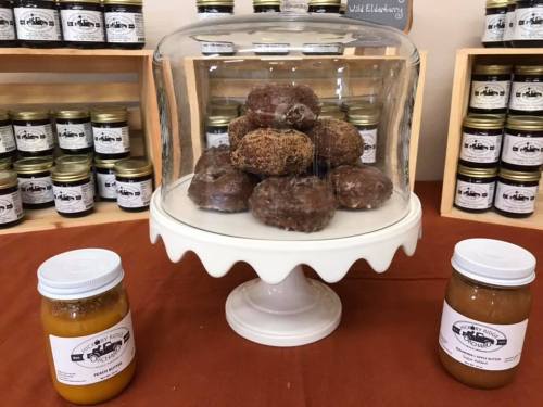 A glass dome covers a display of chocolate truffles on a white cake stand, with jars of preserves on either side.