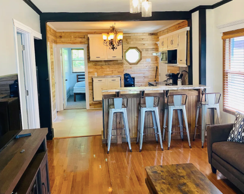 Cozy living space featuring a wooden kitchen, bar stools, and a view of a bedroom through an open doorway.