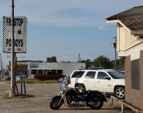 A motorcycle parked in front of a roadside diner with a sign for "First Stop Po' Boys" and nearby vehicles.