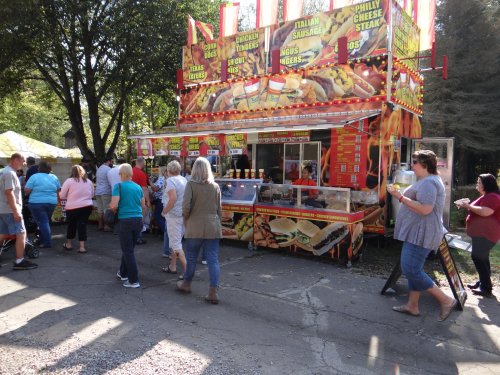 A busy food stand with colorful signage, serving various snacks, as people line up to order. Trees in the background.