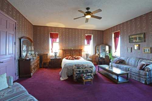 A cozy bedroom with patterned wallpaper, a large bed, a sofa, and wooden furniture, featuring warm lighting and decorative accents.