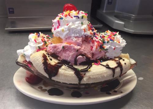 A colorful banana split topped with whipped cream, sprinkles, cherries, and chocolate syrup.