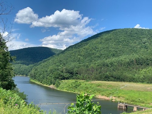 A serene landscape featuring a river surrounded by lush green hills and a blue sky with fluffy clouds.