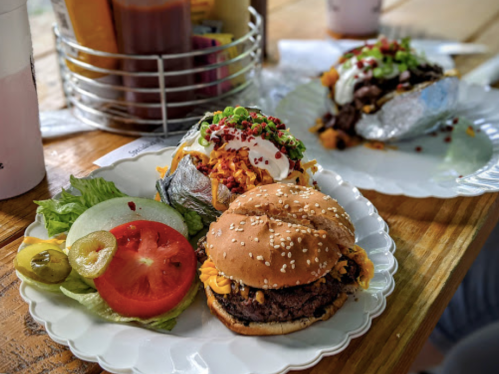 A plate with a burger, lettuce, tomato, and pickles, alongside a baked potato topped with cheese and sour cream.