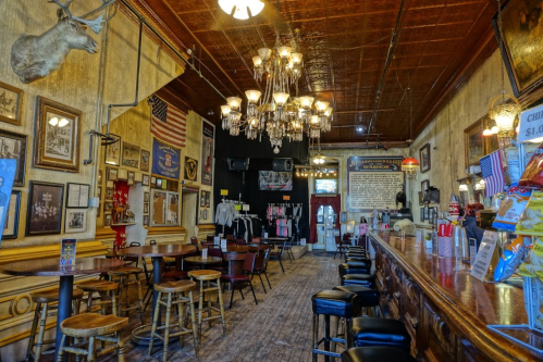 Interior of a vintage bar with wooden furniture, chandeliers, and historical decor, featuring a long bar and seating area.