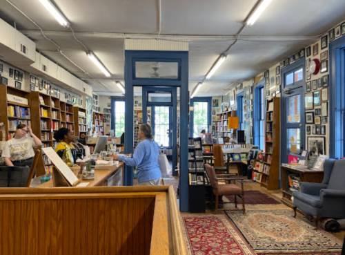 A cozy bookstore interior with bookshelves, a checkout counter, and patrons browsing among framed photos on the walls.