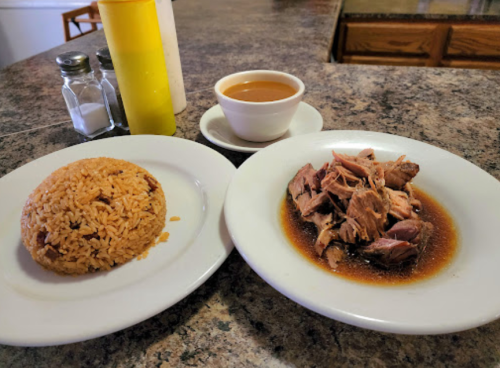A plate of rice and shredded meat in sauce, with a small bowl of broth and condiments in the background.