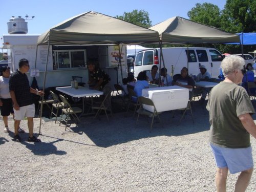 A busy outdoor market scene with tents, tables, and people interacting in a sunny environment.