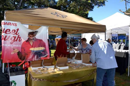 A vendor tent at a market featuring sweet treats, with customers interacting and sampling products.