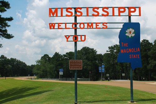 Sign welcoming visitors to Mississippi, featuring "The Magnolia State" and surrounded by trees and a clear sky.