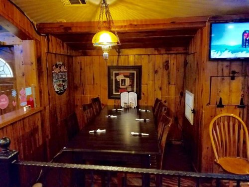 Cozy wooden dining area with a large table, chairs, and warm lighting, featuring a TV and decorative wall art.