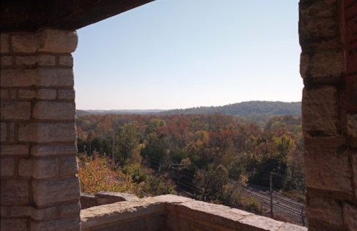 View of colorful autumn trees and distant hills framed by a stone archway, with clear blue sky above.