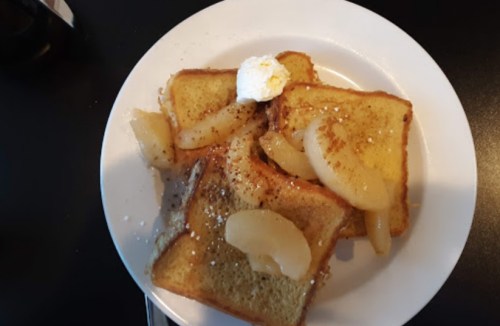 A plate of French toast topped with sliced apples and a dollop of whipped cream.