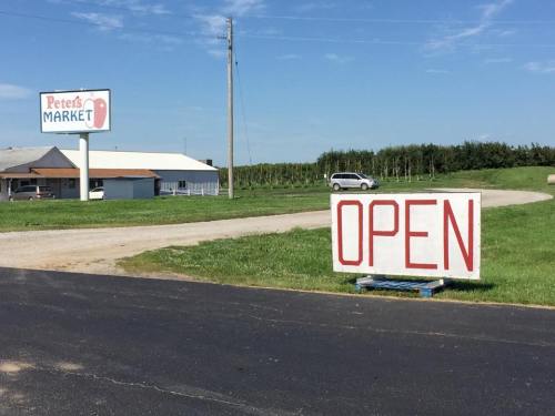 A roadside market with a large "OPEN" sign and a building in the background, surrounded by green fields.