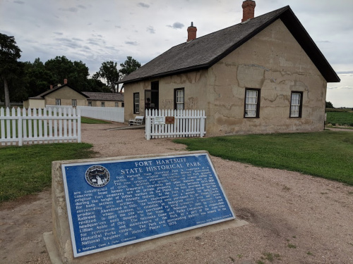 A historic building at Fort Hartsuff State Historical Park, with a blue informational plaque in the foreground.