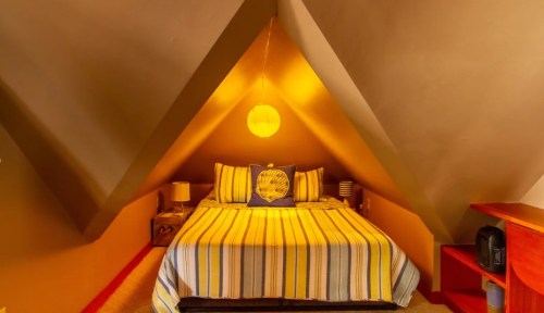 Cozy attic bedroom with a striped bedspread, warm lighting, and sloped walls, creating a snug atmosphere.