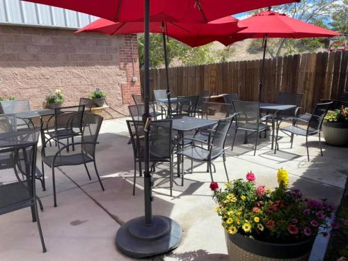 Outdoor patio with red umbrellas, black tables, and chairs surrounded by colorful flower pots and a wooden fence.