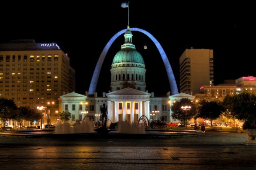 Night view of the Gateway Arch and historic courthouse, illuminated with city lights and a full moon in the background.